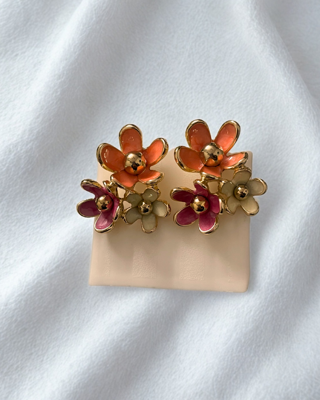 Elegant gold enamel floral stud earrings by KLYAA styled on white fabric