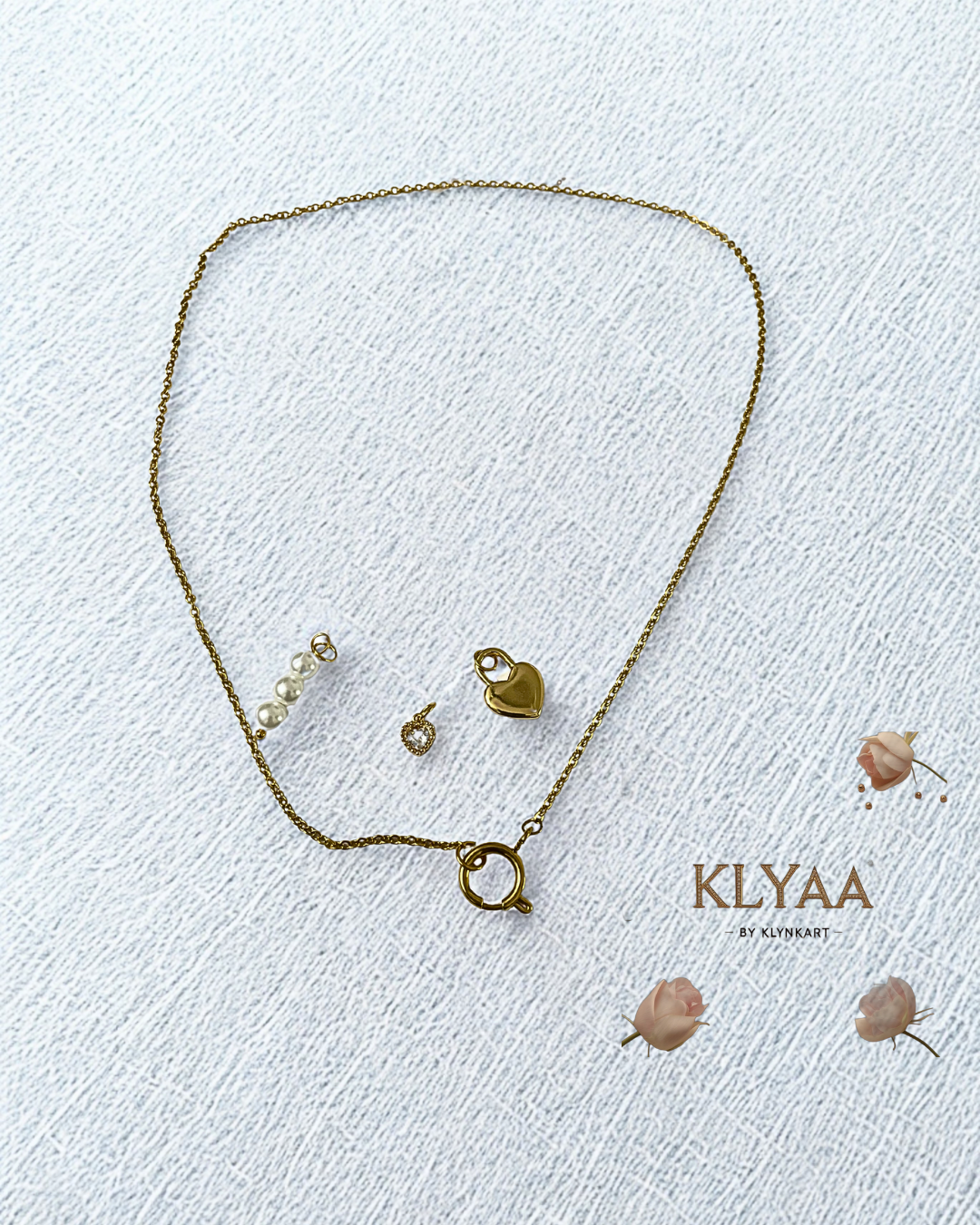 Golden Trinity Chain by KLYAA shown with detachable pearl, gold, and crystal heart charms on fabric background