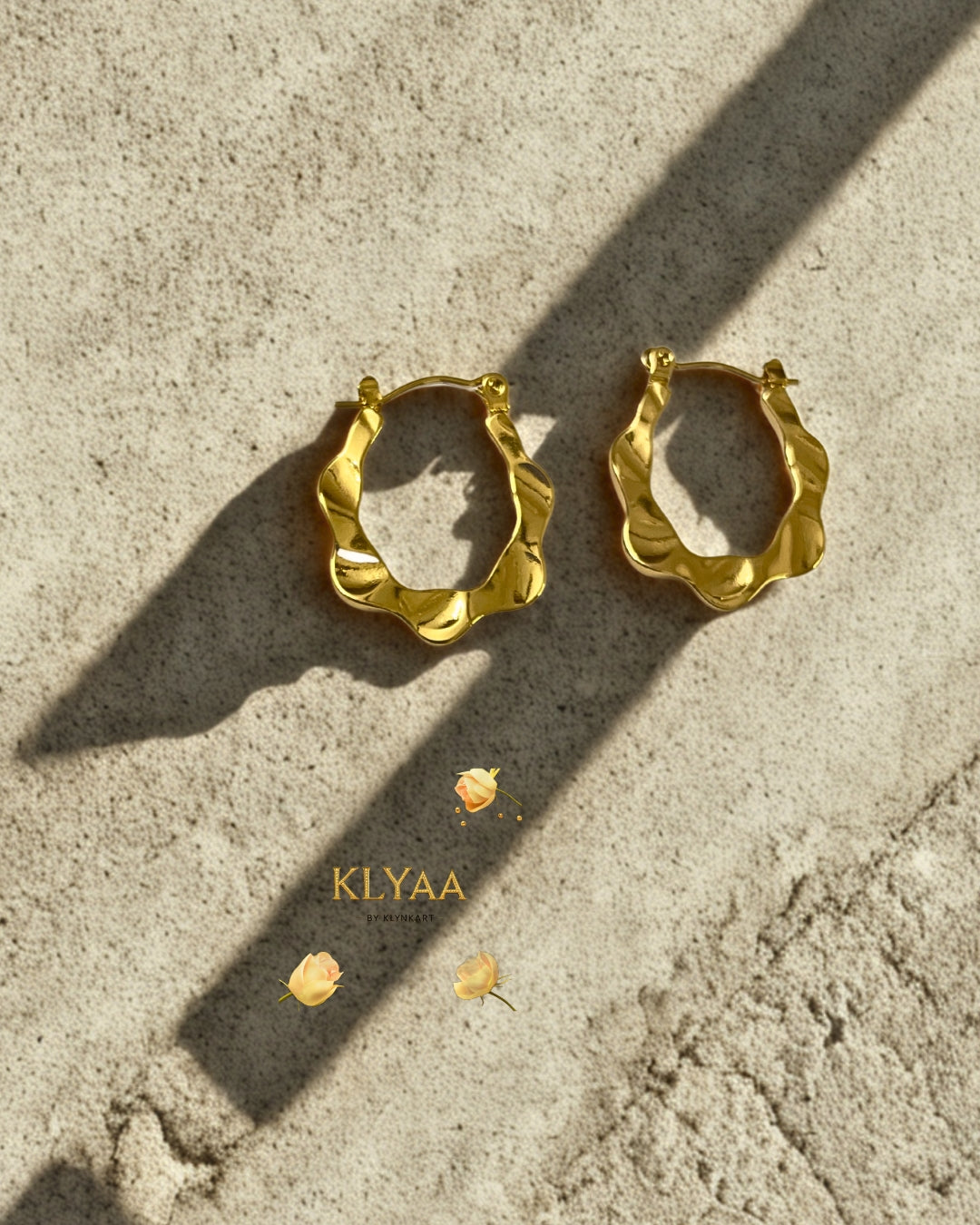 Ripple design sculpted anti-tarnish gold hoops by KLYAA displayed on textured surface