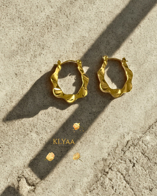 Ripple design sculpted anti-tarnish gold hoops by KLYAA displayed on textured surface