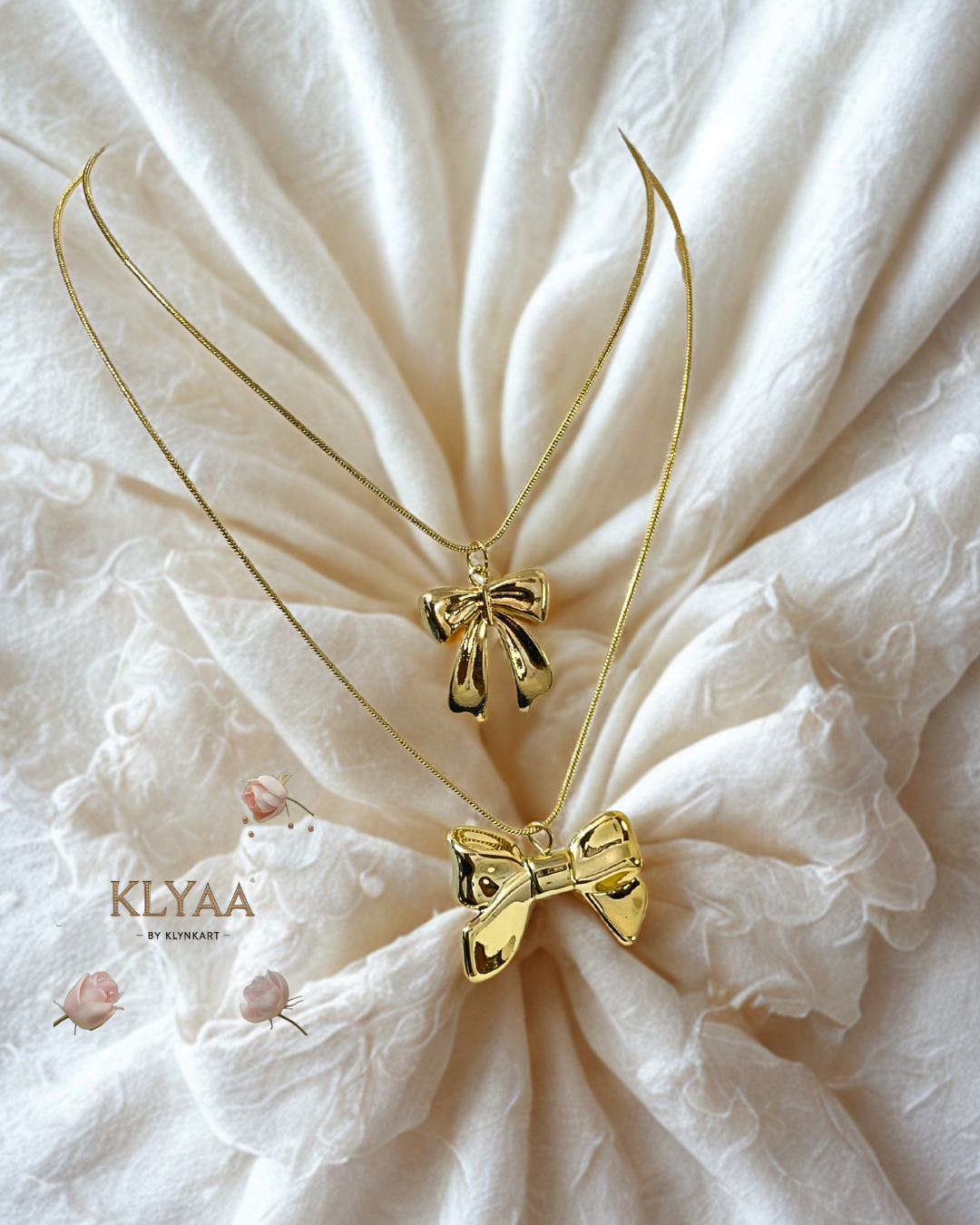 Layered gold chain with two shiny gold bow charms displayed on cream fabric – KLYAA jewellery